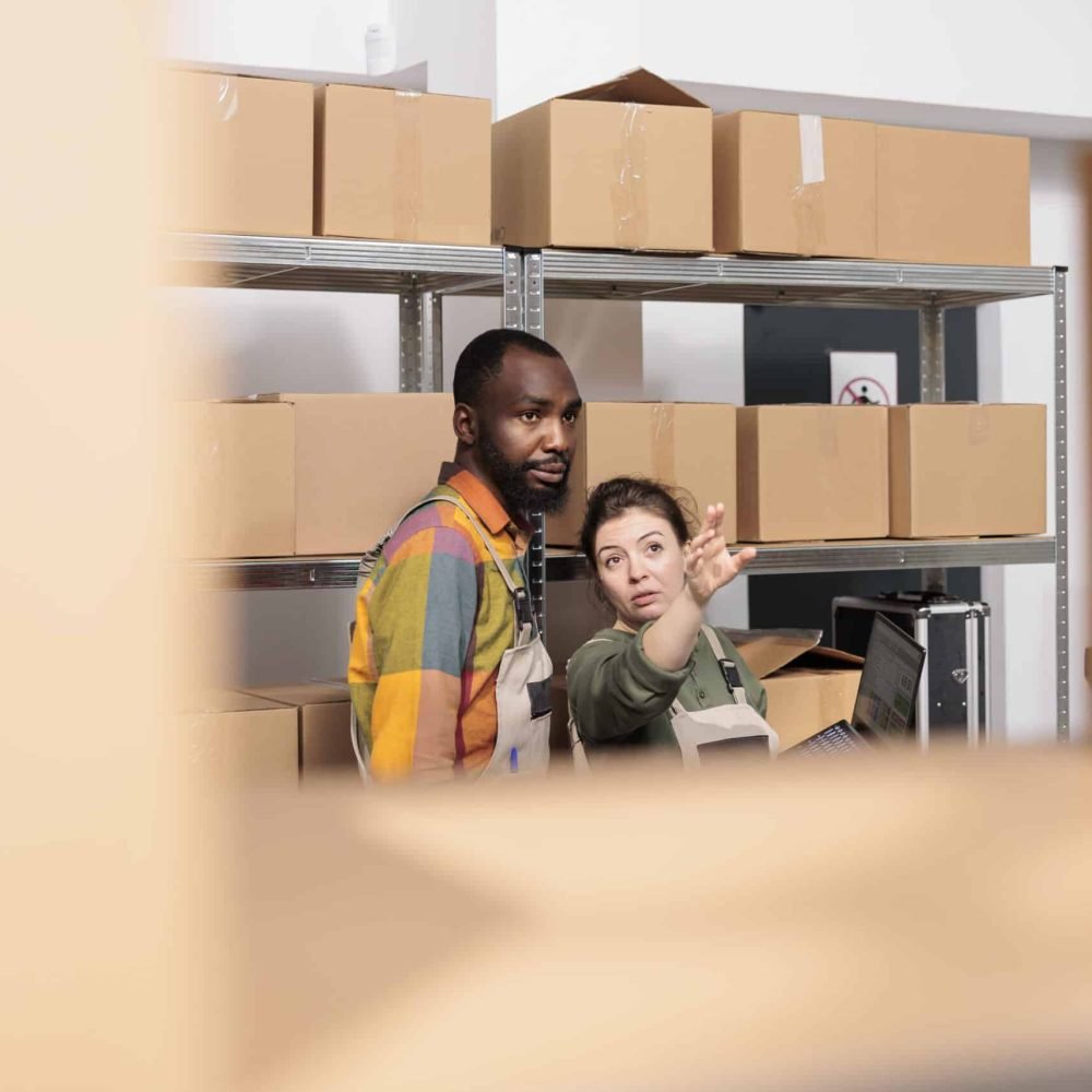 Diverse warehouse managers packing parcels and managing delivery operations. Colleagues working in post office storage, standing beside cardboard boxes shelves preparing orders in storage room